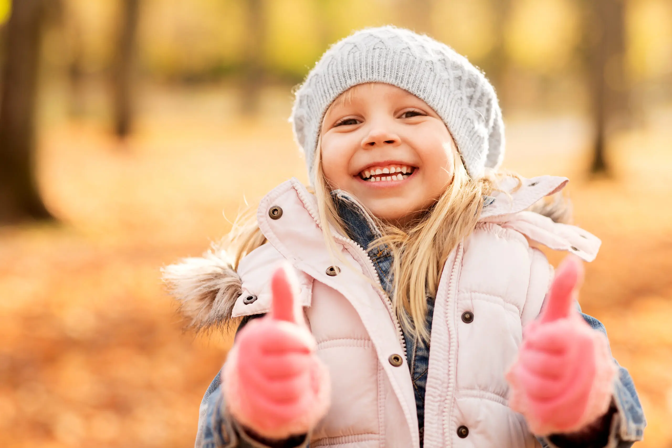 childhood, season and people concept - happy little girl at autumn park showing thumbs up