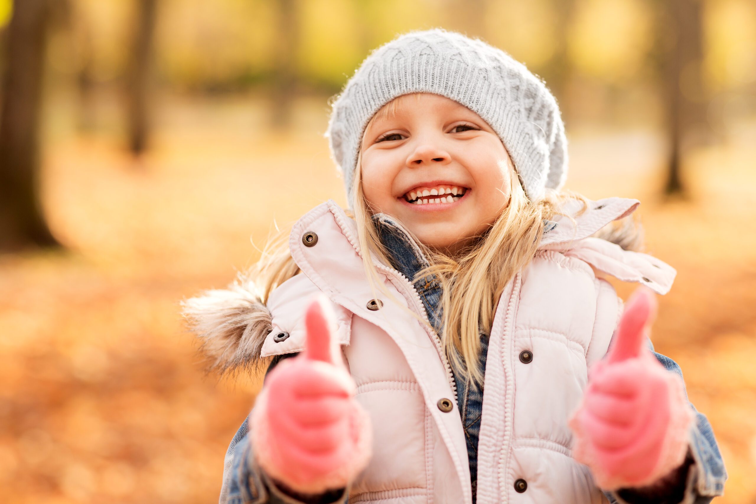 childhood, season and people concept - happy little girl at autumn park showing thumbs up